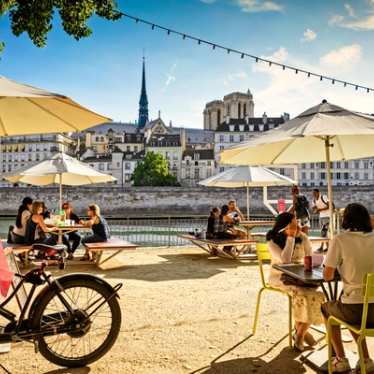 Sommerliche Szene am Seine-Ufer in Paris mit Menschen unter Sonnenschirmen – genießen Sie den Sommer in Frankreich. Nach Paris mit dem Eurostar Zug – entspannt ankommen und den Moment genießen.