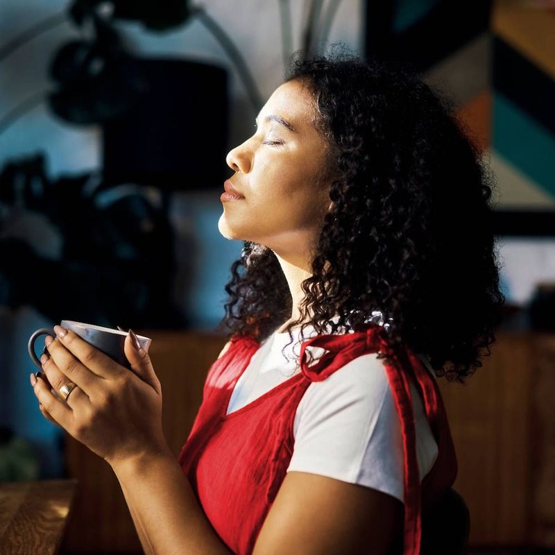 A woman closing her eyes enjoying coffee, feeling focused and peaceful