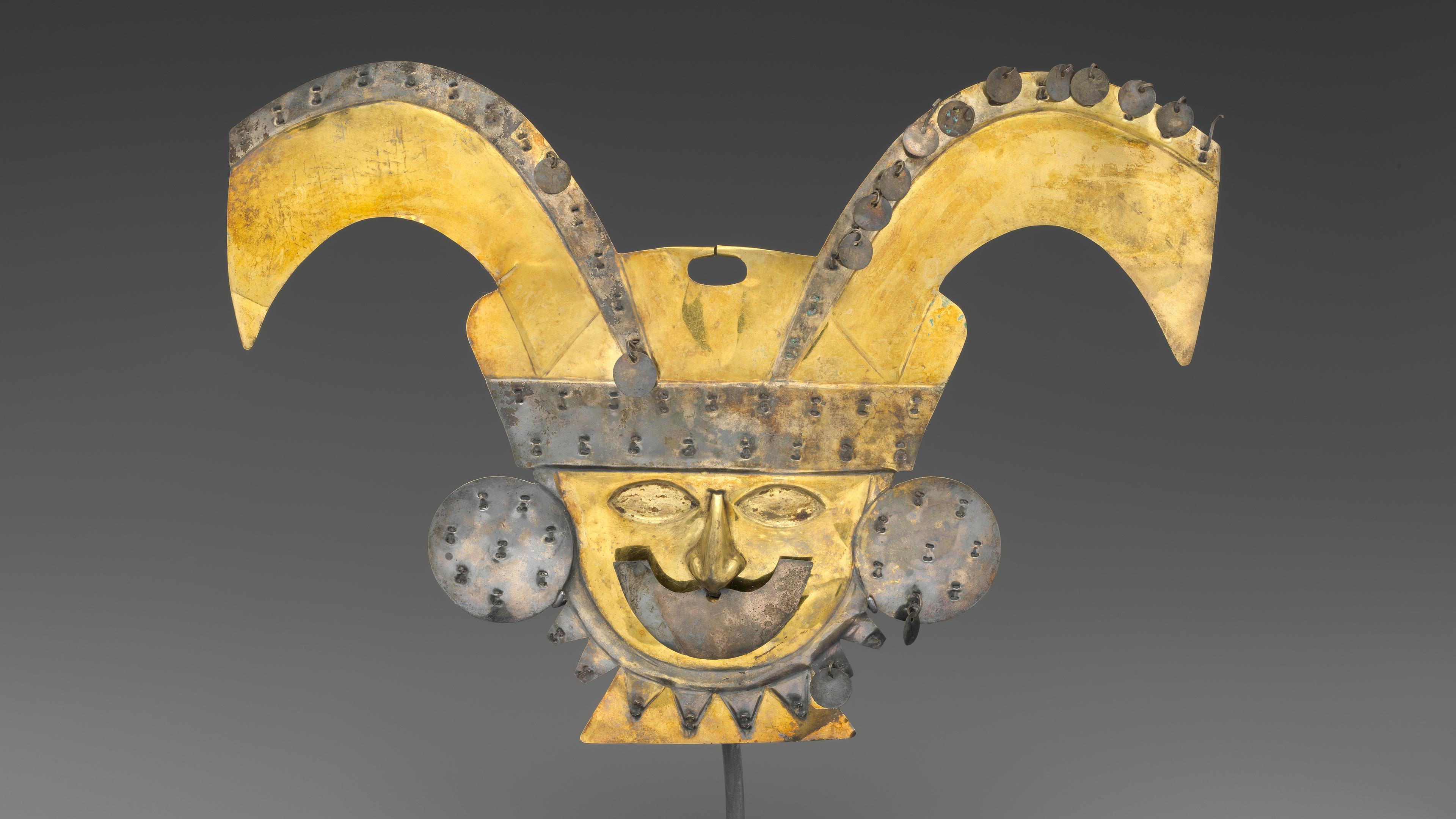 Gold and silver nose ornament in the shape of a face wearing a crescent-shaped nose ornament, large earspools, and a turbaned headdress