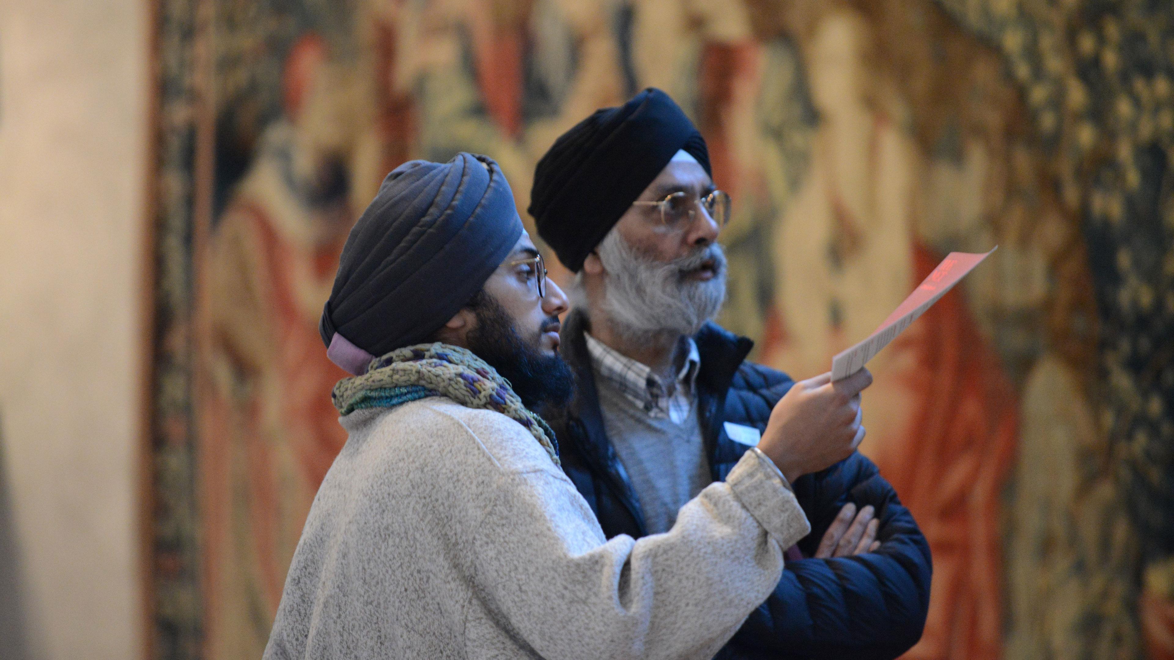 Two visitors stand before a tapestry, closely examining the details
