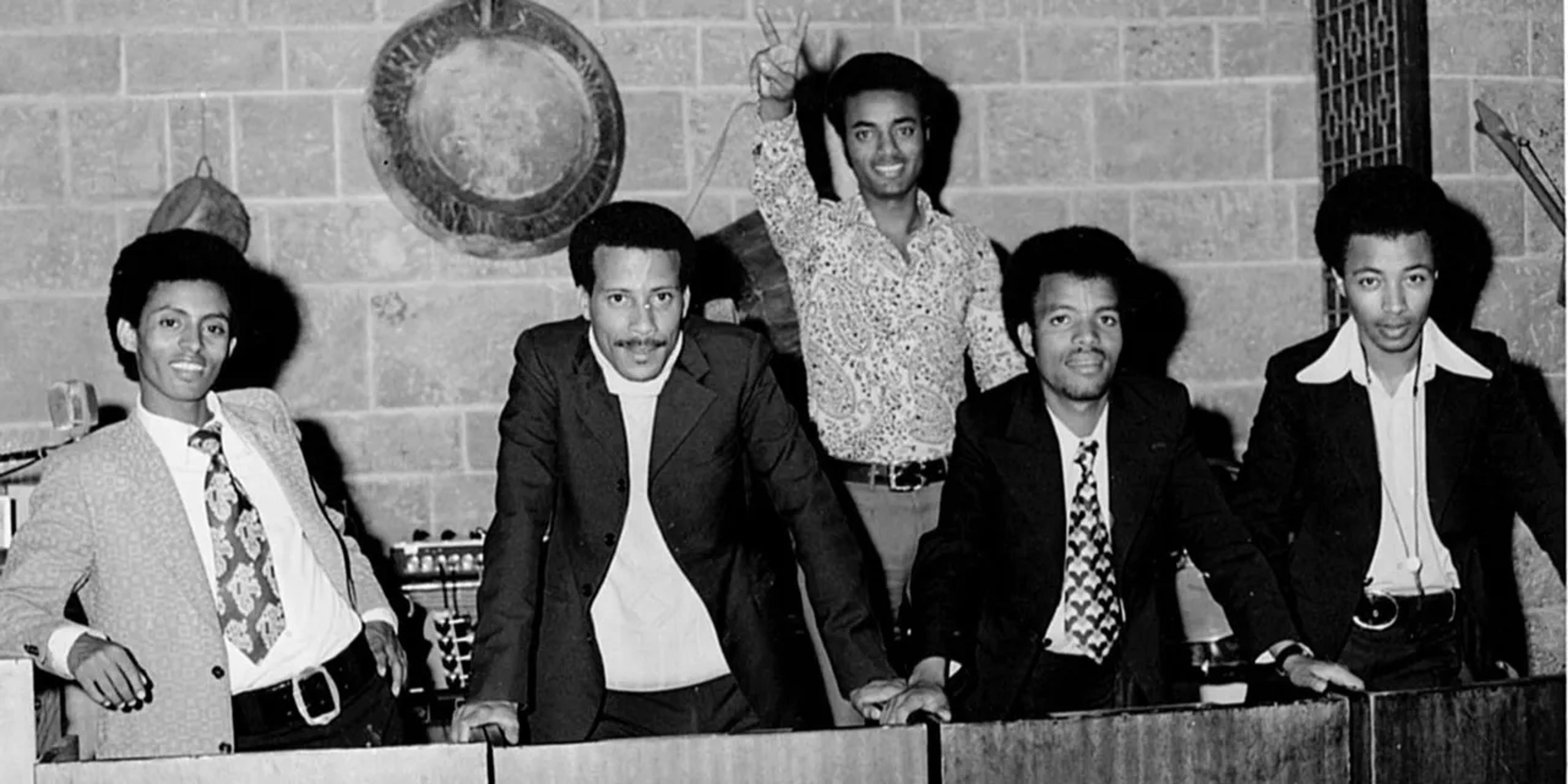 Black and white image of 5 men of color, each looking at the camera, each wearing suits. 