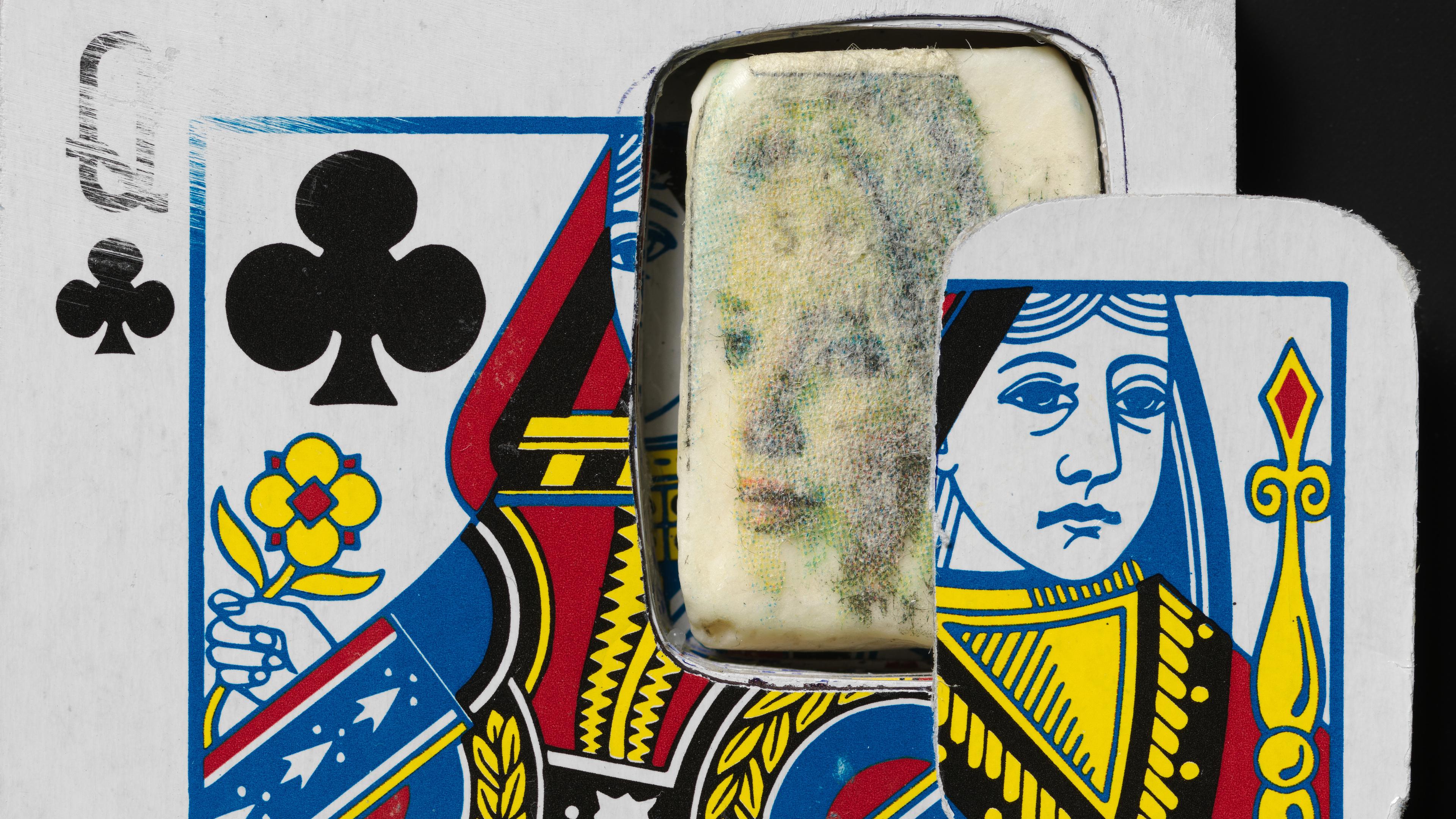 Close-up of a Queen of Clubs playing card with a cut-out section. Behind it, a faded, ghostly face is visible, creating a surreal, mysterious mood.