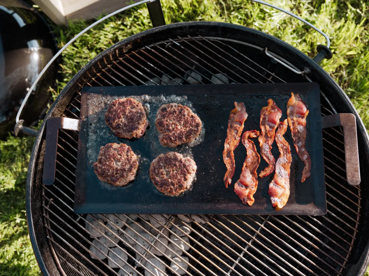 Burgers and bacon strips are being cooked on a salt block over a charcoal grill.