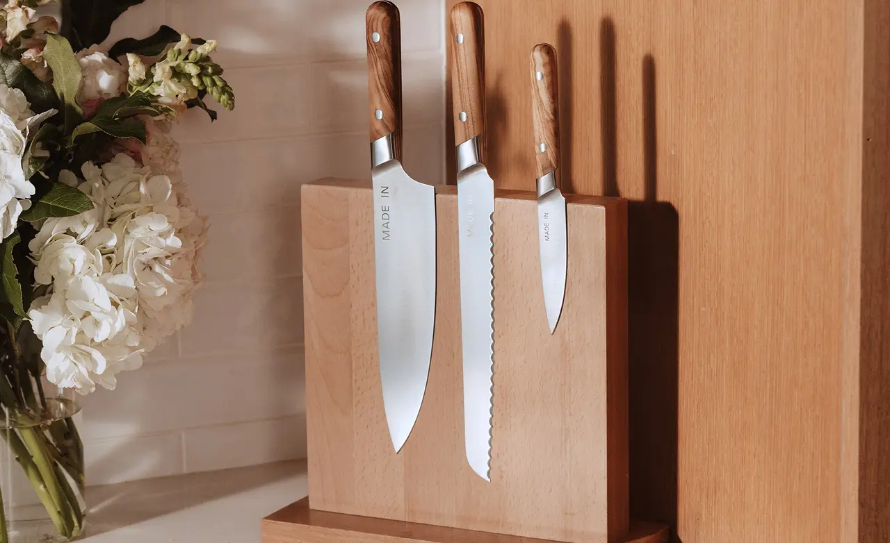 A wooden knife block displays three kitchen knives of varying sizes, with sleek metal blades and wooden handles, alongside a vase of flowers.